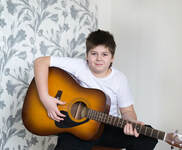 Teenage boy guitar student holding his acoustic guitar and posing for the camera.