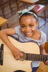 Young female guitar student holding acoustic guitar and smiling for her picture during her guitar lesson. 