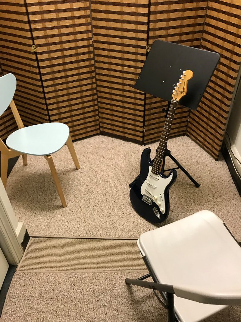 Guitar lesson room with fender stratocaster, music stands, and guitar stools.