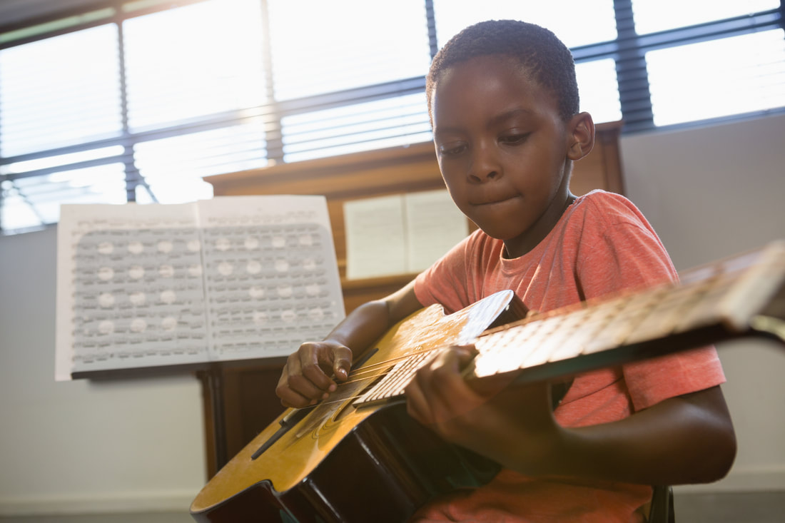 Young boy playing guitar and practicing guitar music at his lesson.