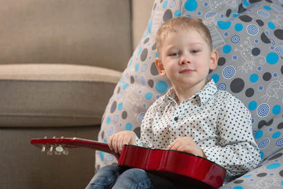 Young boy holding his guitar and looking at the camera after his guitar lesson at Providence Guitar Academy.