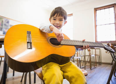 Young male guitar student holding his guitar at his lesson at Providence Guitar Academy. He is happy to be playing guitar.